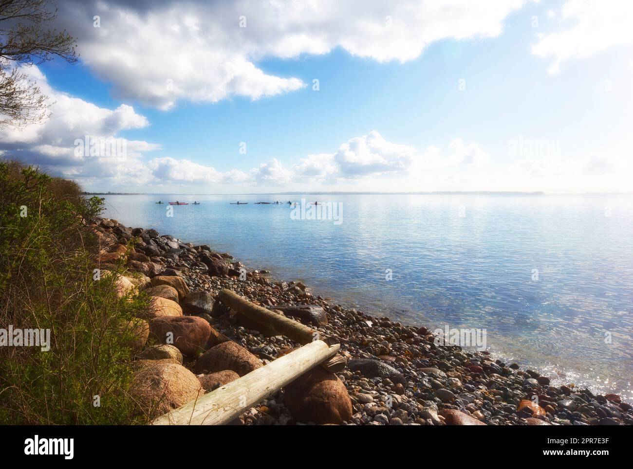 Copyspace auf See mit felsigem Ufer und wolkigem Himmelshintergrund. Ruhige Meereswellen an einer Küste mit Kajaks am Horizont. Malerische Landschaft für einen friedlichen Sommerurlaub Stockfoto