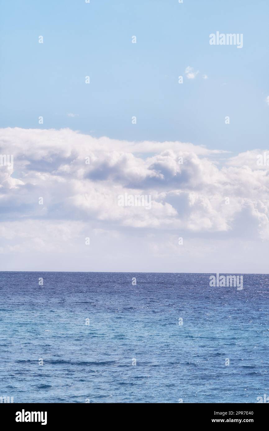 Ein wolkiger blauer Himmel und ein friedlicher, ruhiger Ozean, getrennt durch einen wunderschönen Horizont mit Kopierbereich. Tiefblaues Wasser unter einer Wolkenlandschaft. Die vielen Gezeiten, Strömungen und Wellen im weiten offenen Meer Stockfoto