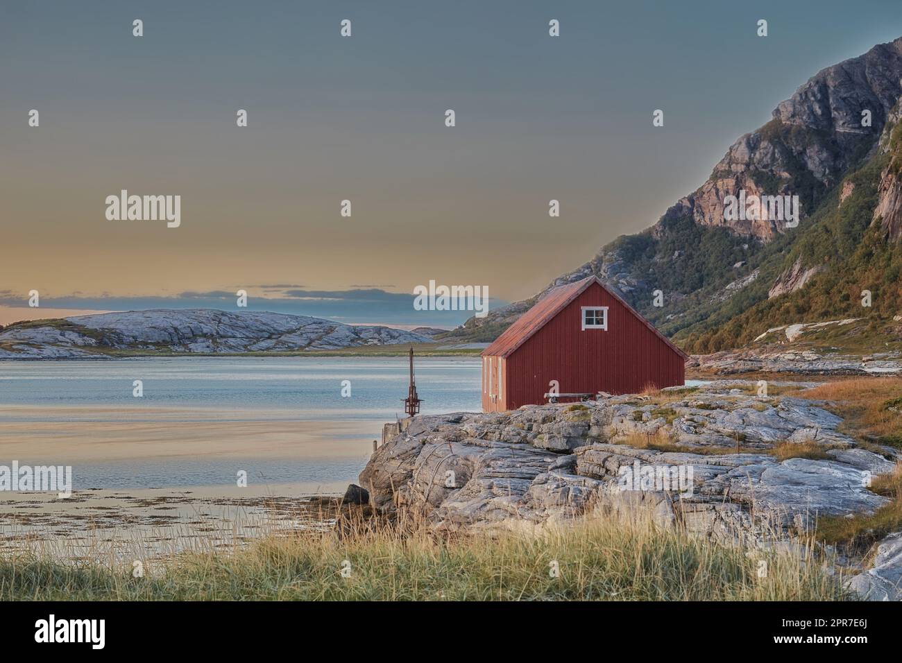 Malerischer Blick auf verlassenes Seehaus oder Hütte in einer abgelegenen und felsigen Landschaft. Natürliche Wildnis um eine kleine Wasserbucht in Norwegen. Landschaft und Meereslandschaft eines Ozeans oder Meeres mit blauem Himmel Stockfoto