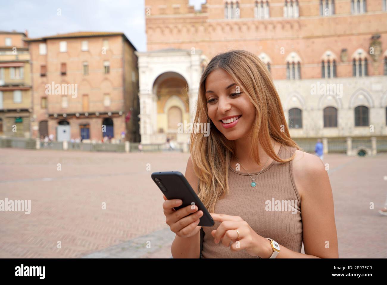 Porträt einer glücklichen jungen Frau, die mit dem Finger auf dem Smartphone durch die historische Stadt Italien scrollt Stockfoto