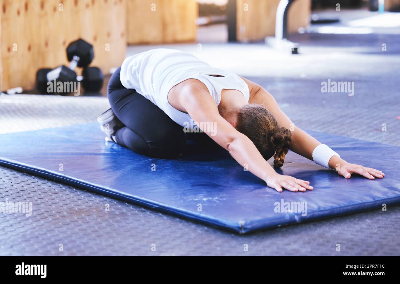 Biegen und strecken, um die Gesundheit zu verbessern. Aufnahme einer sportlichen jungen Frau, die beim Training im Fitnessstudio eine Kinderpose macht. Stockfoto