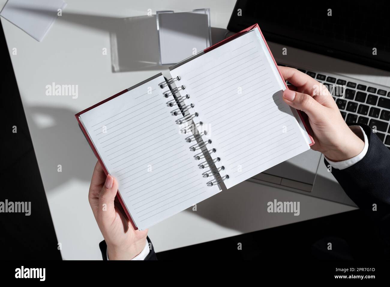 Geschäftsfrau, Die Ein Notizbuch Mit Neuen Ideen Über Dem Schreibtisch Mit Notizen Und Laptops In Der Hand Hat. Frau Im Anzug Mit Notizblock Mit Wichtigen Nachrichten Über Dem Tisch Mit Memos Und Computer. Stockfoto