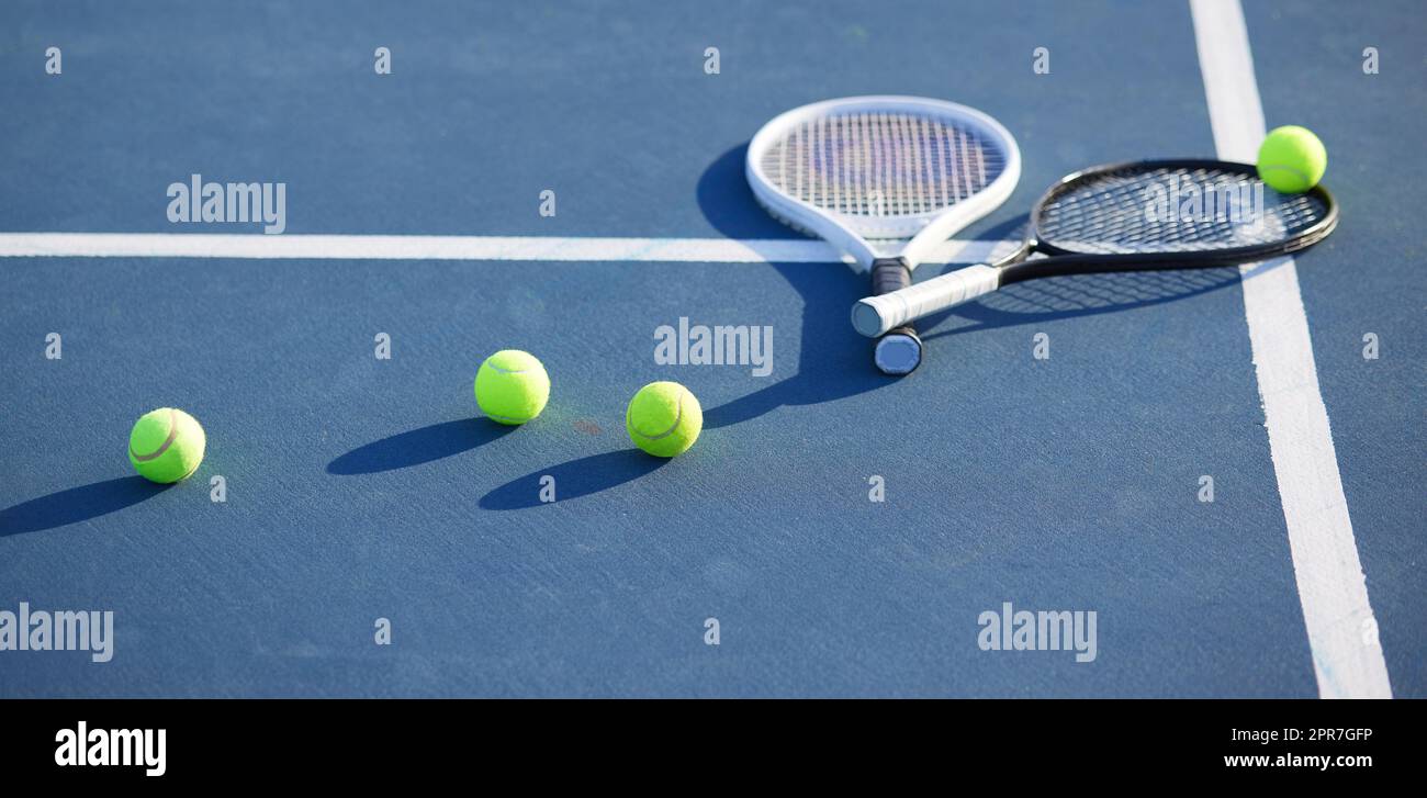 Ist diese Gesundheit, die Ihren Namen ruft. Aufnahme von zwei Tennisschlägern und Tennisbällen auf einem Platz während des Tages. Stockfoto