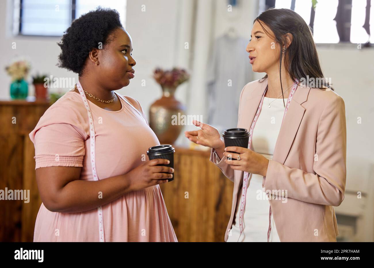 Denken wir über einen zweiten Standort nach: Zwei attraktive junge Geschäftseigentümerinnen, die Kaffee trinken, während sie in ihrem Geschäft stehen. Stockfoto