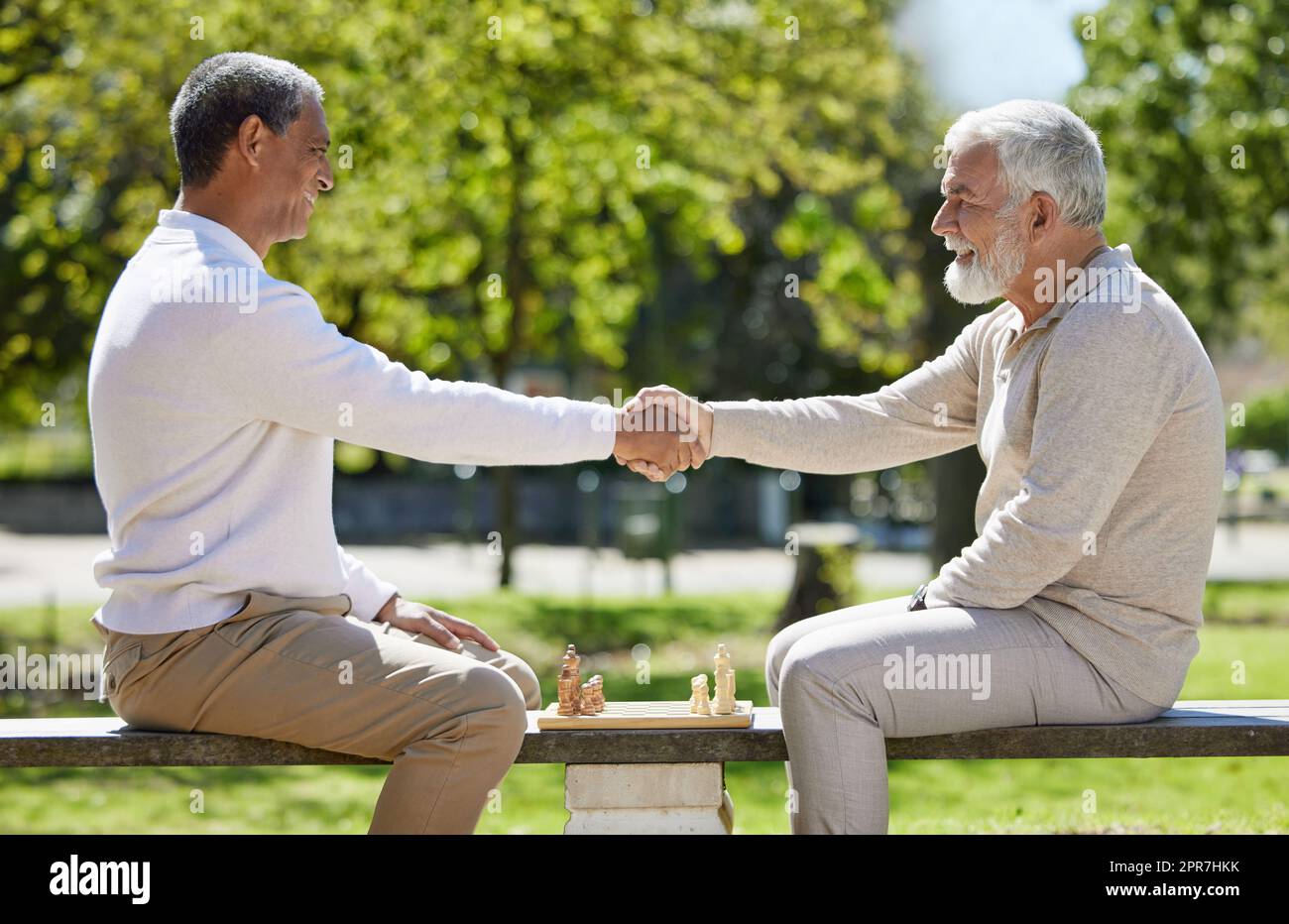 Möge der beste Mann gewinnen. Zwei ältere Männer sitzen zusammen auf einer Bank im Park und schütteln die Hände, bevor sie Schach spielen. Stockfoto
