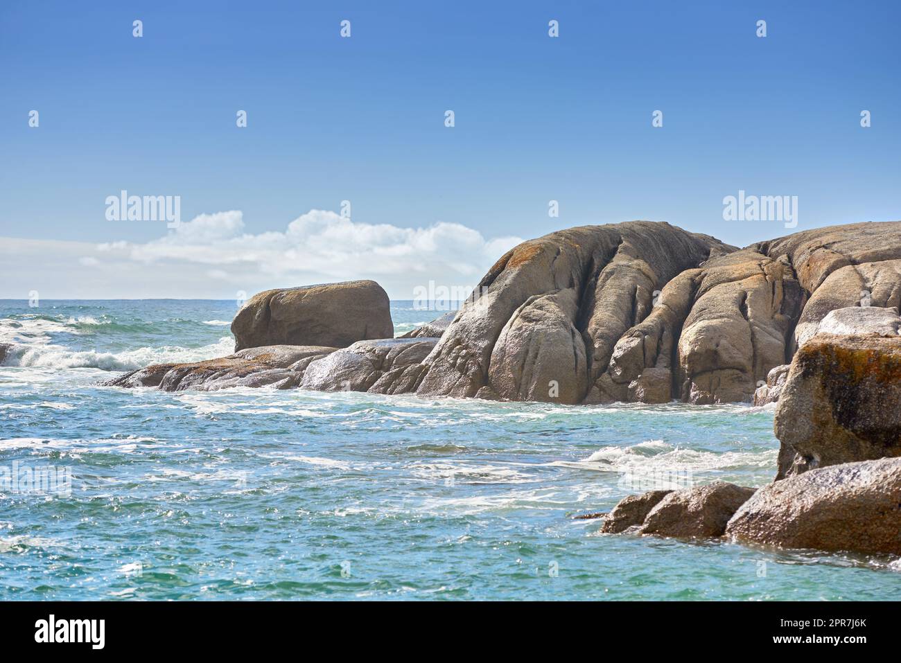 Kopieren Sie Platz auf dem Meer mit einem wolkenlosen blauen Himmelshintergrund und felsiger Küste in Camps Bay, Kapstadt, Südafrika. Felsbrocken an einem Strandufer über einem majestätischen Ozean. Malerische Landschaft für einen Sommerurlaub Stockfoto