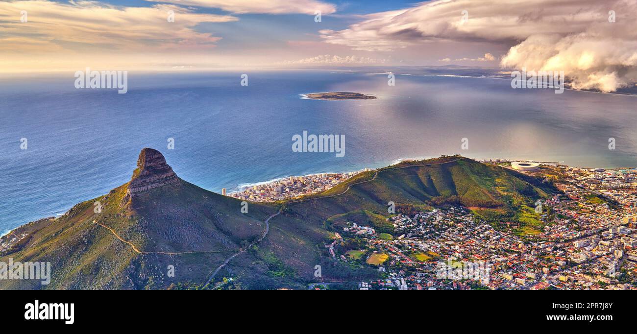 Blick aus der Vogelperspektive auf den Lions Head Mountain mit dem Meer und Wolkendecke. Wunderschöne Landschaft mit grünen Bergen und viel Vegetation rund um eine Stadt in Kapstadt, Südafrika Stockfoto