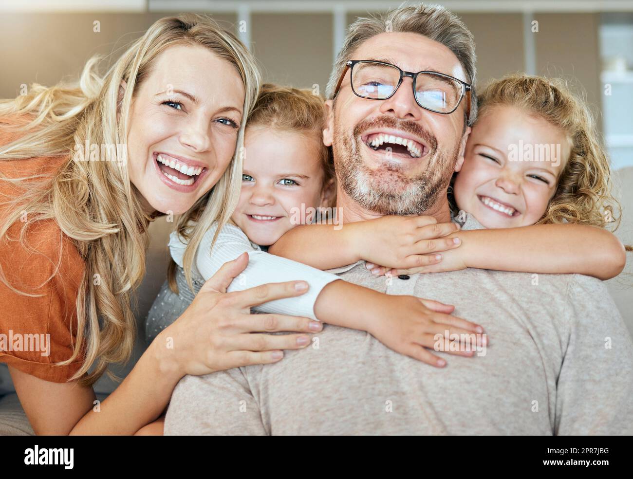 Porträt einer glücklichen kaukasischen vierköpfigen Familie, die sich zu Hause im Wohnzimmer entspannen kann. Liebend lächelnde Familie, liebevoll zusammen. Ein junges Paar, das sich mit seinen kleinen Kindern zu Hause anfreundet Stockfoto