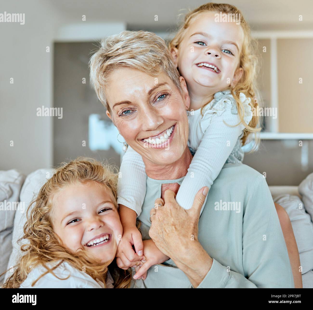 Porträt einer mehrgenerationsübergreifenden Familie von drei Frauen, die sich nur gemeinsam auf dem Sofa entspannen. Lächelnde Oma, die ihre beiden Enkelinnen zu Hause Babysitting Stockfoto