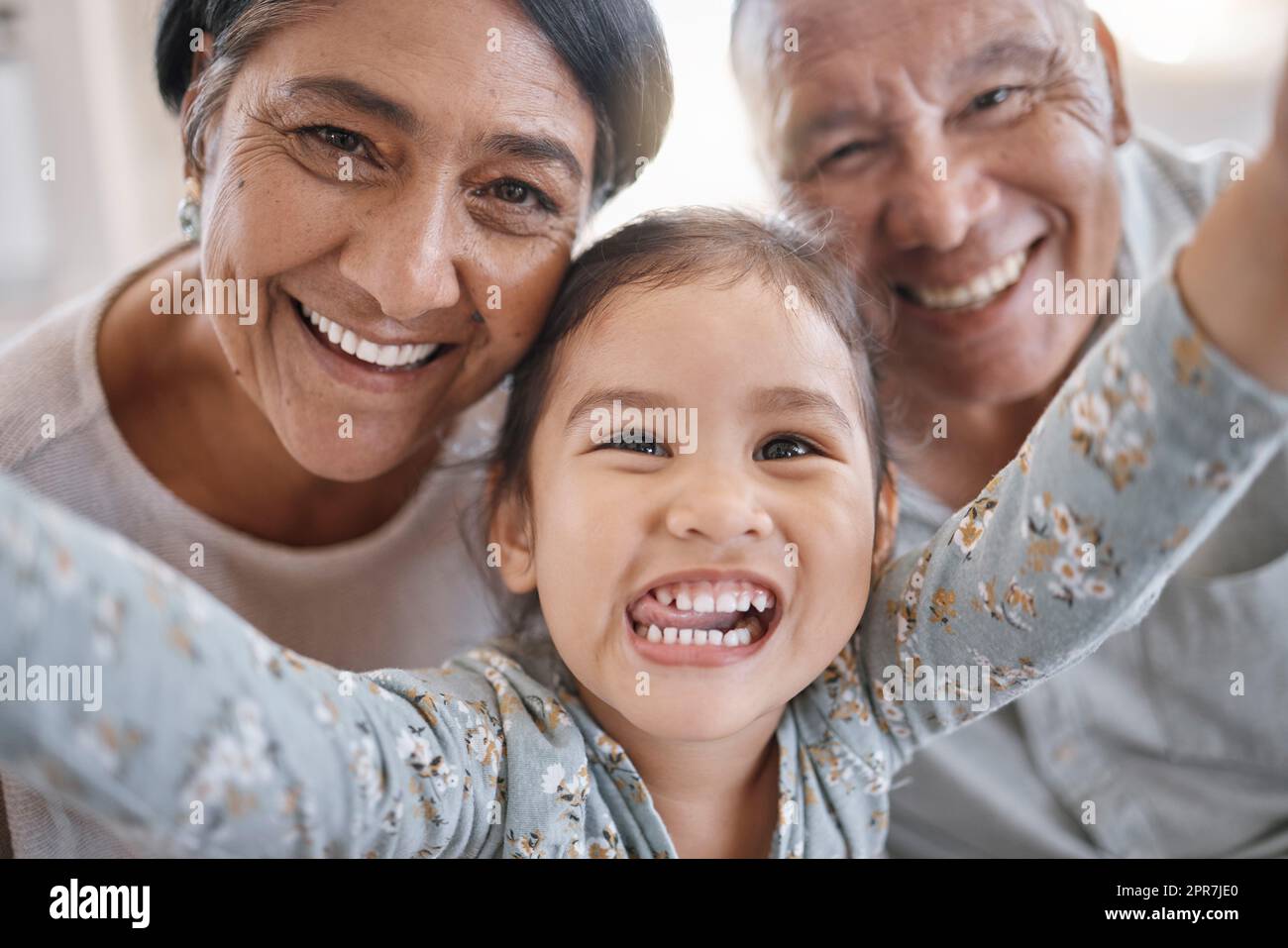 Porträt von lächelnden Großeltern und Enkelkindern gemischter Rassen, die zu Hause in der Lounge ein Selfie machen. Lateinamerikanischer Seniorenmann und -Frau, die Fotos macht und sich mit ihrer süßen kleinen Enkelin zu Hause anfreundet Stockfoto