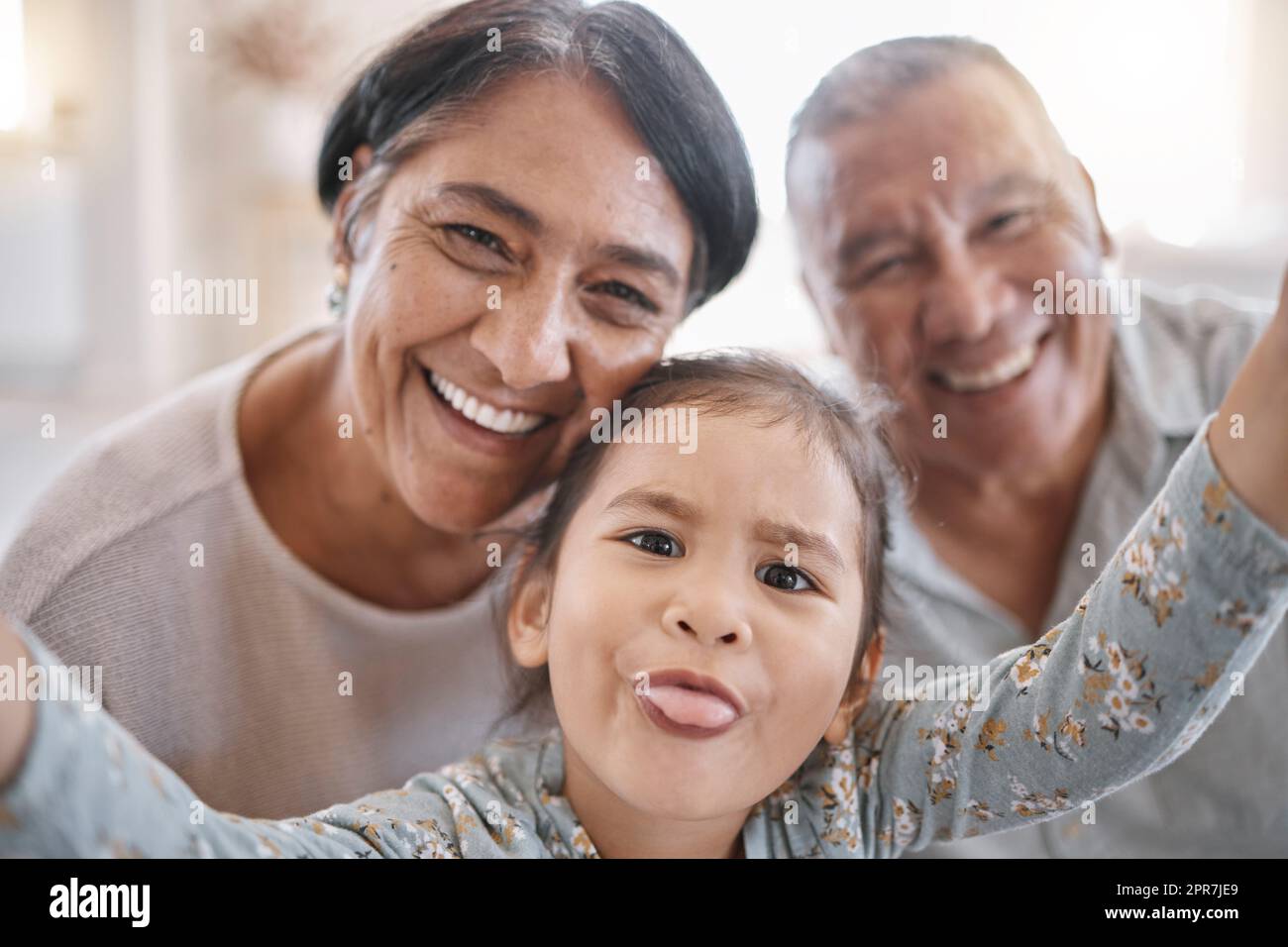 Porträt von lächelnden Großeltern und Enkelkindern gemischter Rassen, die zu Hause in der Lounge ein Selfie machen. Lateinamerikanischer Seniorenmann und -Frau, die Fotos macht und sich mit ihrer süßen kleinen Enkelin zu Hause anfreundet Stockfoto