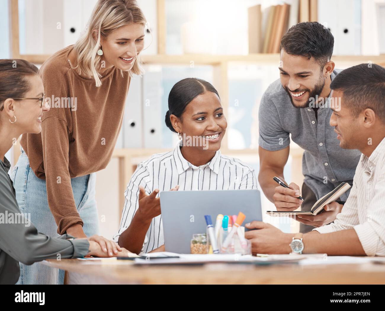 Eine Gruppe glücklicher und vielfältiger Kollegen, die in einem Konferenzraum im Büro gemeinsam auf einem Laptop diskutieren. Treffen einer Geschäftsfrau mit gemischten Rassen, um ihrem Team in einer kreativen Startup-Agentur Ideen und Strategien zu erläutern Stockfoto