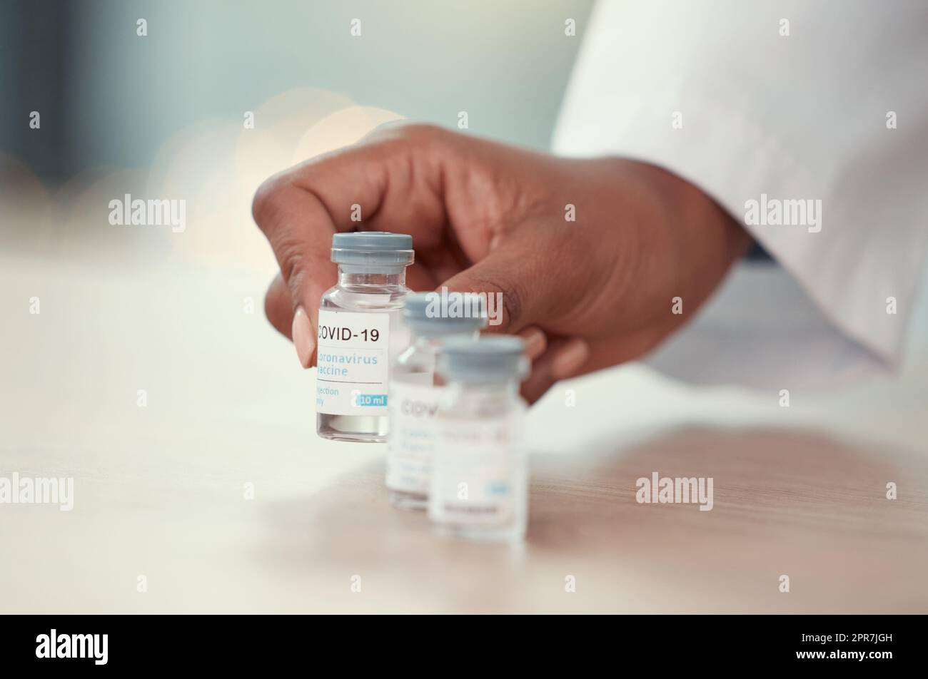 Nahaufnahme eines Arztes, der Flaschen Covid-Impfstoff auf den Tisch stellt. Hände eines Arztes mit Corona-Virus-Antidot. Medizinisches Fachpersonal stellt Medizin auf den Tisch. Die Hände eines hausarztes, der ein kovides Heilmittel hält Stockfoto