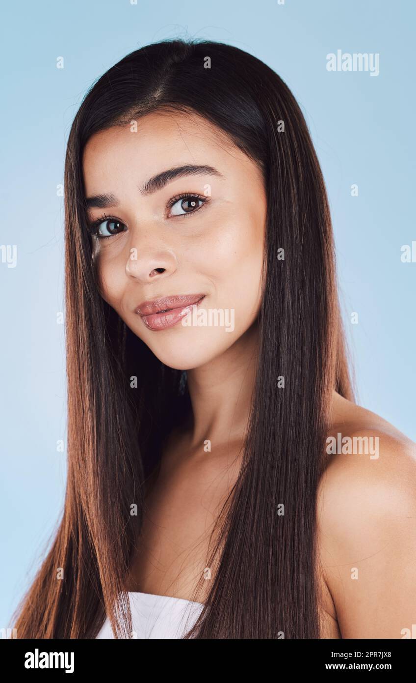 Porträt einer wunderschönen jungen hispanikerin mit gesunder Haut und schlankem, langem Haar, das vor einem blauen Studiohintergrund lächelt. Glückliches Mixed Racing Model mit makellosem Teint und natürlicher Schönheit Stockfoto
