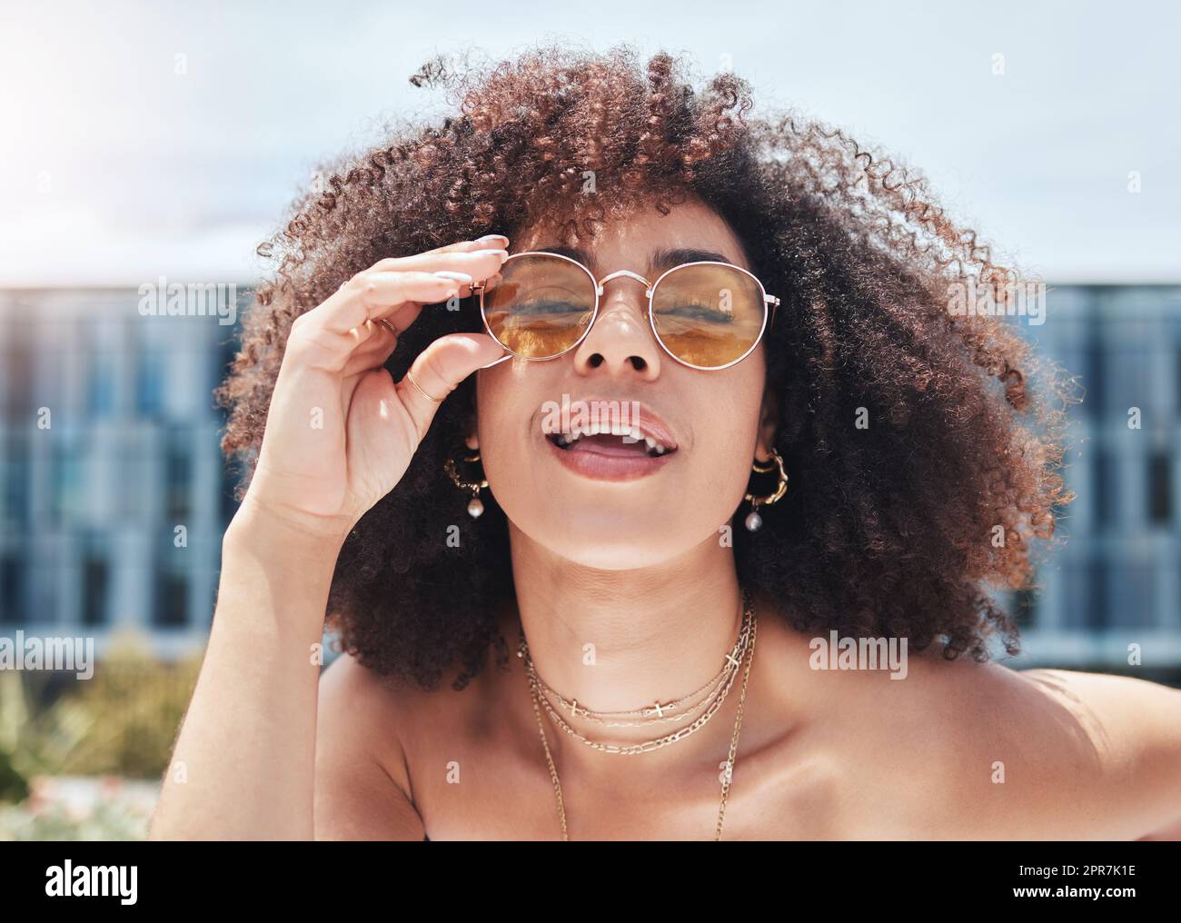 Junge Mischrasse mit lockigem, natürlichem Afrohaar und trendiger, stilvoller Sonnenbrille. Eine Frau sieht nur sorglos, cool und selbstbewusst aus. Fröhliche, modische hispanische Frau in der Stadt Stockfoto