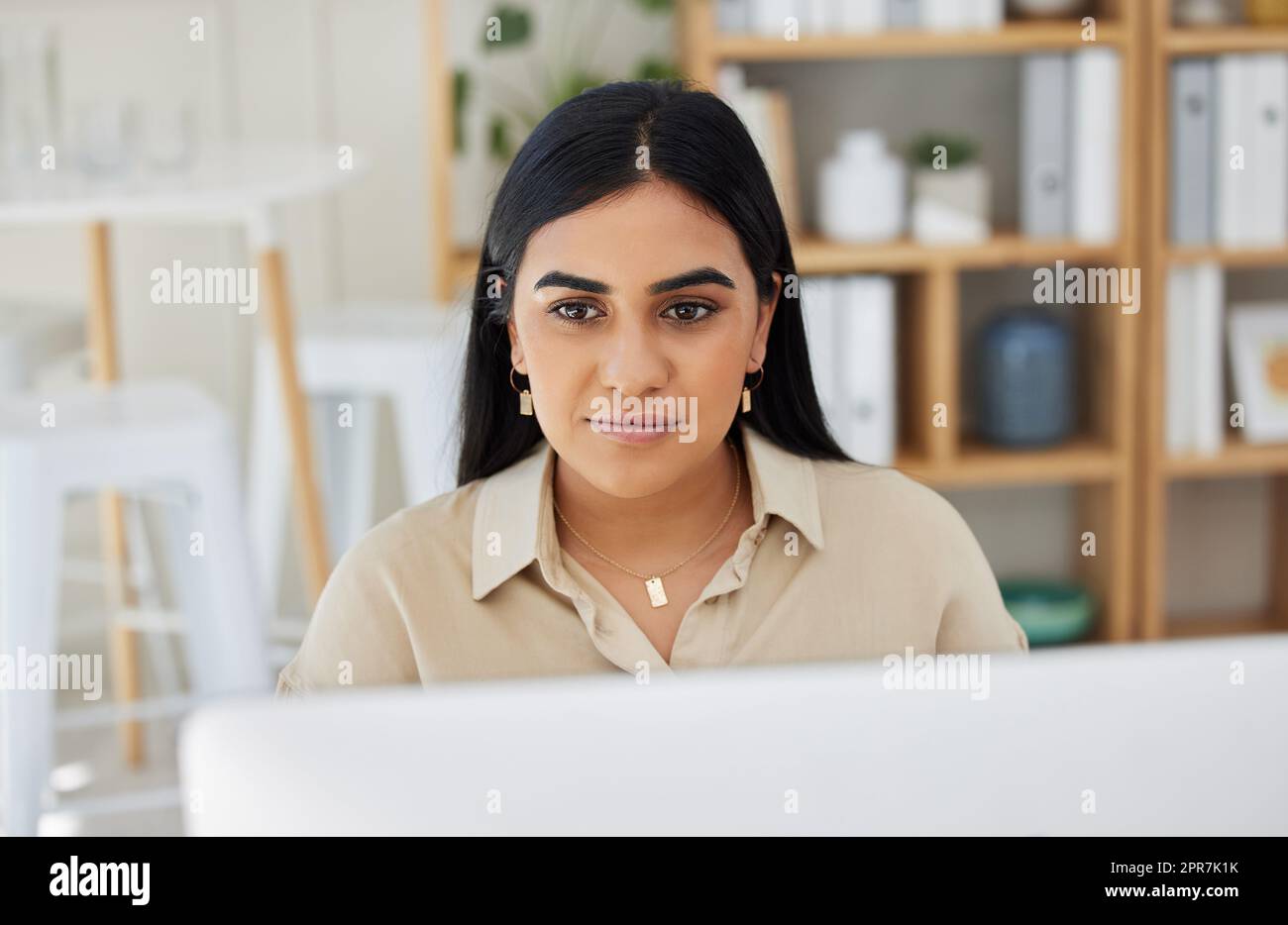 Eine wunderschöne junge Geschäftsfrau gemischter Rassen, die an ihrem Computer im Büro arbeitet. Selbstbewusste und erfolgreiche Unternehmerin indischer Herkunft, die an ihrem Arbeitsplatz auf einem Desktop arbeitet. Stockfoto