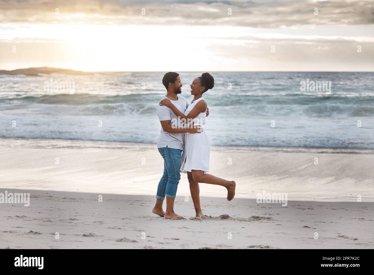 Ein verspieltes afroamerikanisches Paar, das einen Tag am Meer verbringt. Sorgenfreier Freund und Freundin tanzen am Strand. Liebevoller Mann und Frau, die sich am Meer anfreunden Stockfoto