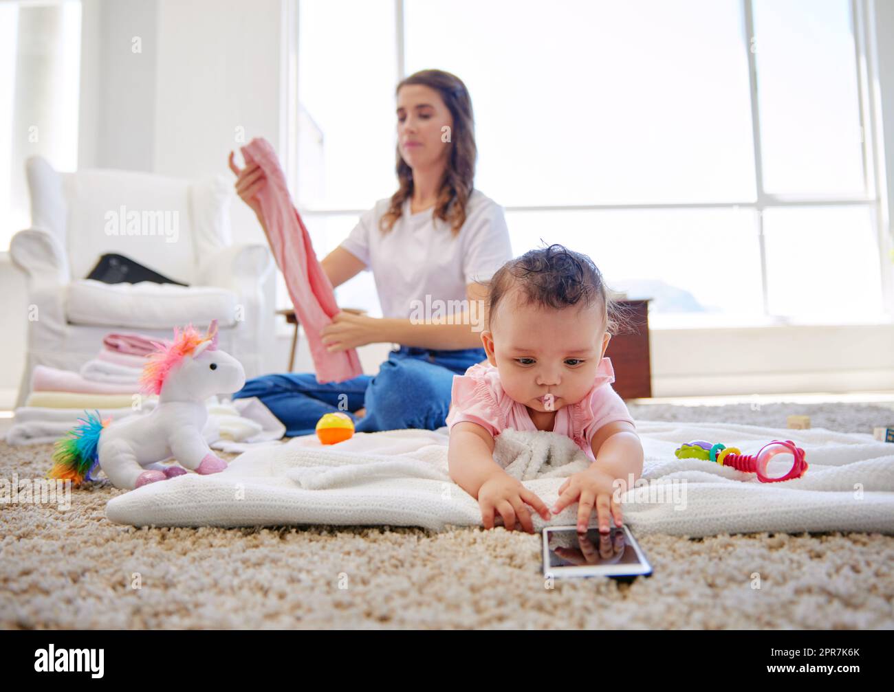 Das wird immer mehr zu einem Kampf jeden Tag. Eine Mutter faltet Kleidung, während ihr Baby in der Lounge spielt. Stockfoto