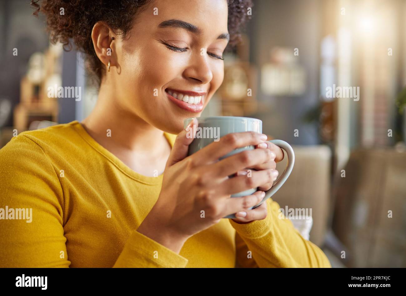 Junge, fröhliche Mischrasse Frau, die zu Hause eine Tasse Kaffee hält und trinkt. Eine gemütliche hispanische Frau lächelt und genießt eine Tasse Tee, während Sie sich zu Hause entspannen Stockfoto
