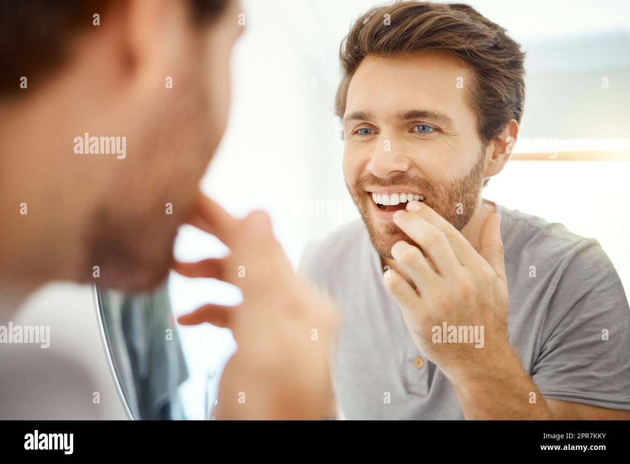 Ein hübscher Mann, der seine Zähne in einem Badezimmer zu Hause überprüft. Kaukasischer Mann, der seine Zähne putzt und in seinem Apartment in einen Spiegel schaut. Stockfoto