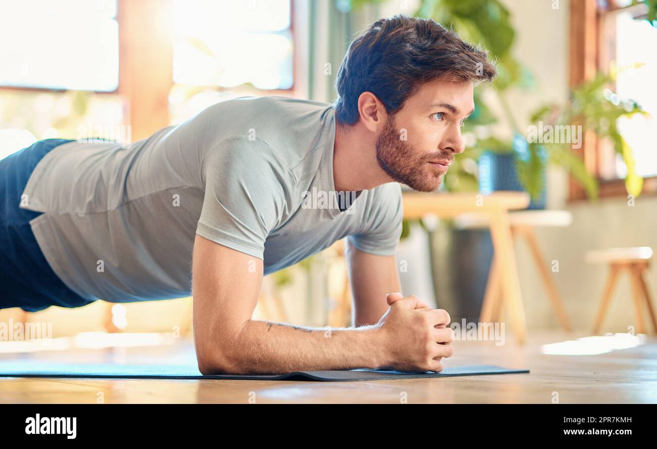 Ein passender junger weißer Mann, der Ellenbogen-Plank macht, hält das Körpergewicht beim Training zu Hause. Fokussierter Kerl fordert sich selbst heraus, Muskeln zu gewinnen, Oberkörper, Kernkraft zu verbessern und die Ausdauer beim Workout zu erhöhen Stockfoto