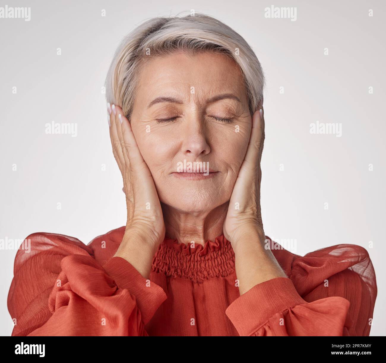 Eine reife Frau, die Kopfschmerzen hat und gestresst aussieht, während sie vor einem grauen Hintergrund posiert. Alternde Frau, die Angst und Angst in einem Studio erlebt Stockfoto