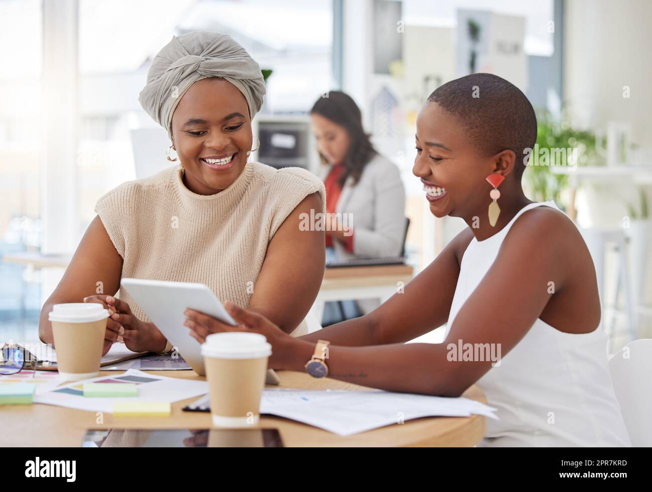 Lächelnde afroamerikanische Geschäftsfrauen sitzen zusammen und verwenden ein digitales Tablet während eines Brainstormings im Büro. Zuversichtlich glückliche schwarze Profis, die eine Strategie mit Technologie planen Stockfoto