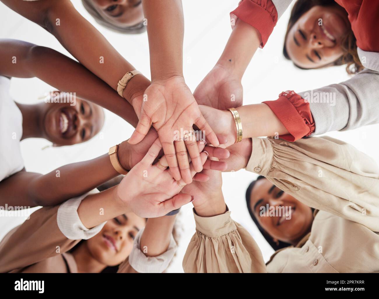 Kleine, vielfältige Gruppe ehrgeiziger, lächelnder Geschäftsfrauen, zusammengedrängt mit Händen in der Mitte. Lächeln, ethnisches Team aus professionellen Kollegen, die sich motiviert, vereint, unterstützt und bereit fühlen Stockfoto