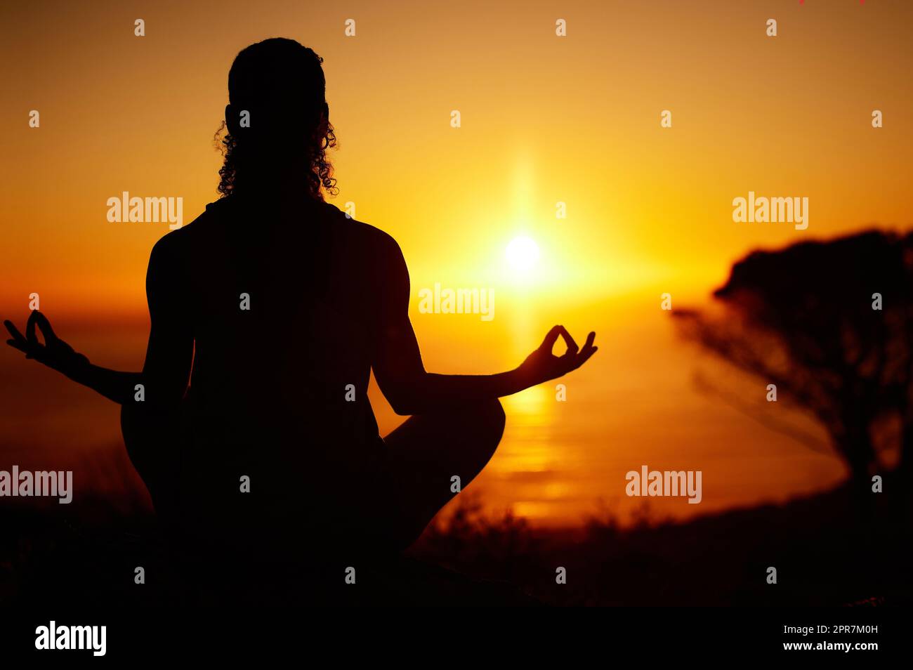 Yoga-Frau mit überkreuzten Beinen meditiert nach hinten für Outdoor-Übungen in abgelegener Natur. Aufmerksame Person, die allein sitzt und für die psychische Gesundheit bei Sonnenuntergang balanciert. Ruhe und Zen in Lotus-Pose Stockfoto