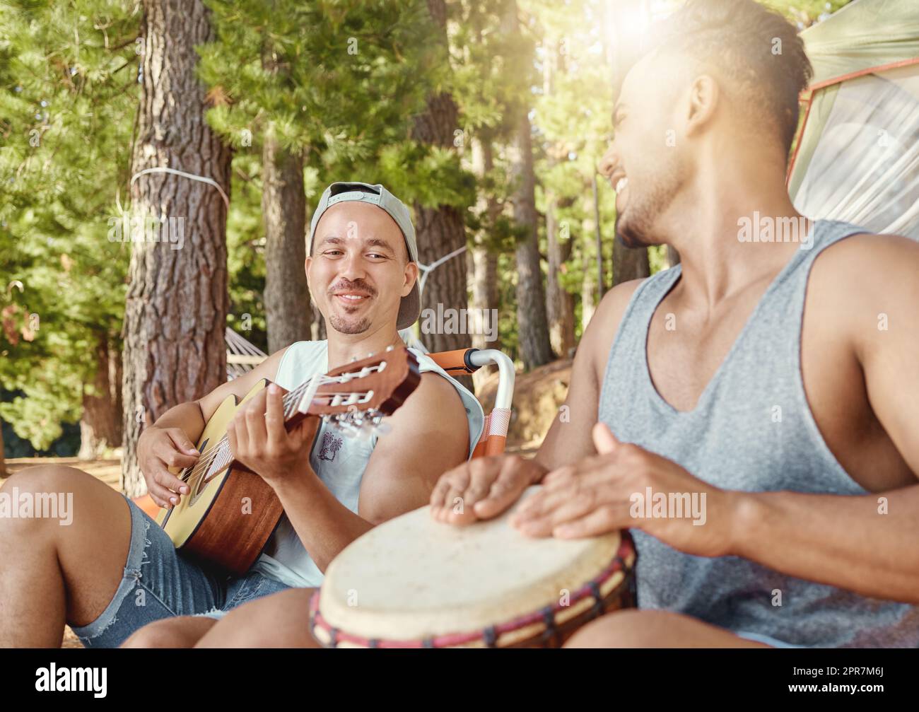 Musik machen im Wald. Zwei junge Männer sitzen und spielen Musikinstrumente während eines Campingausflugs im Wald. Stockfoto