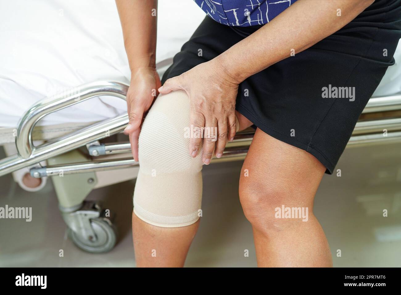 Asiatische ältere Frau trägt elastische Stützkniestütze zur Schmerzlinderung. Stockfoto