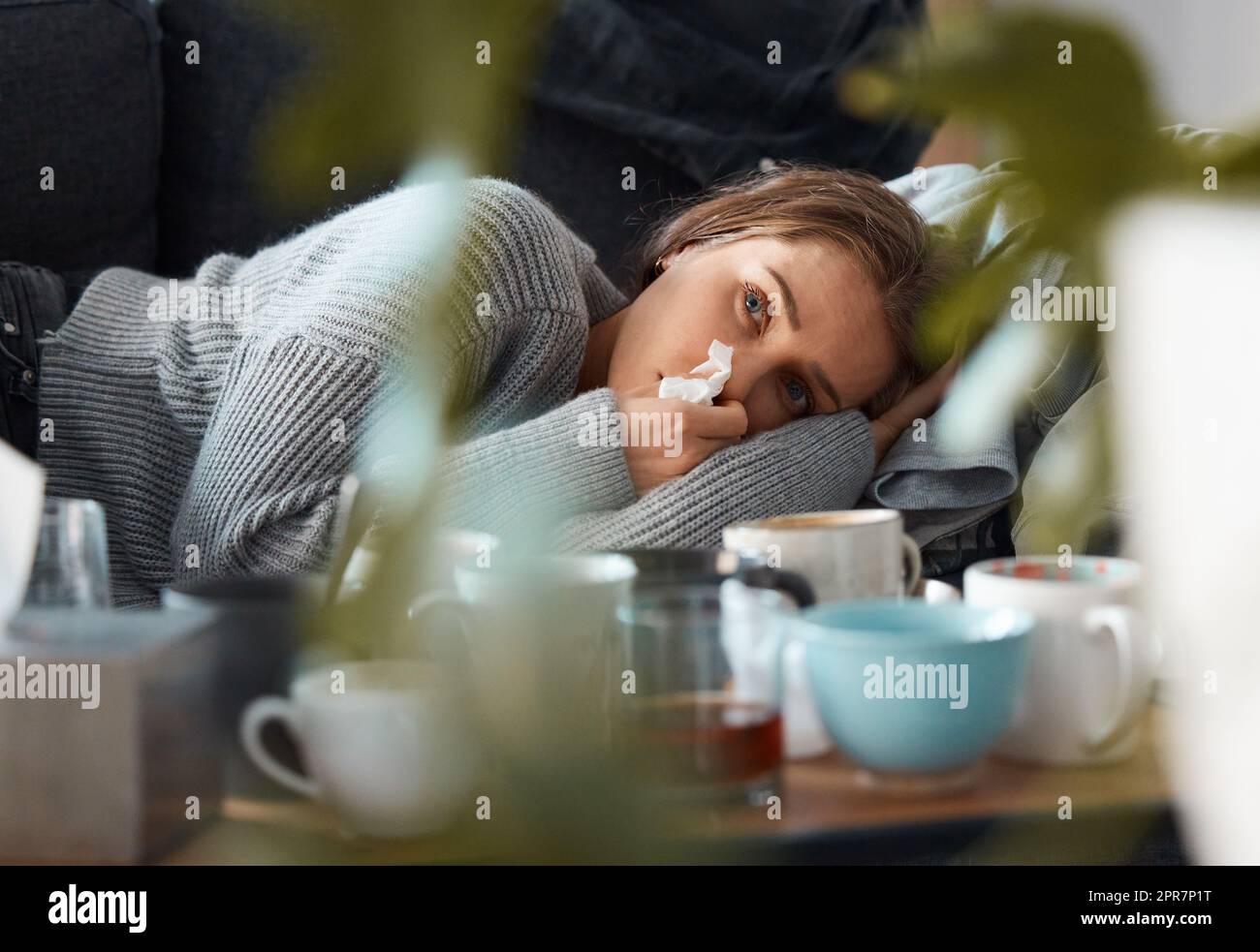 Tage wie diese sind die schlimmsten. Aufnahme einer jungen Frau, die auf ihrer Couch liegt und ihre Nase bläst und deprimiert aussieht. Stockfoto