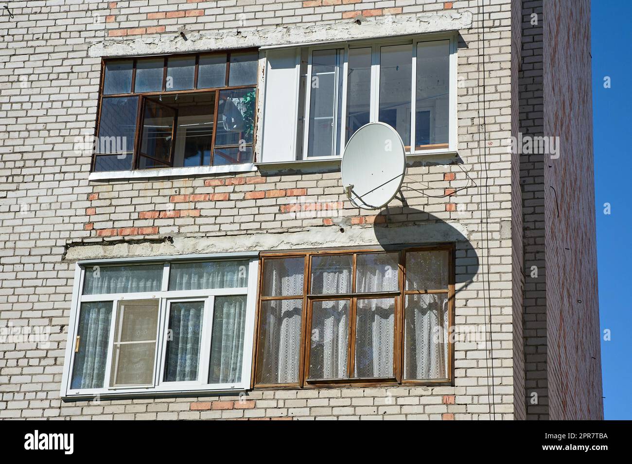 Eine Satellitenschüssel hängt an der Wand eines Backsteinhauses Stockfoto