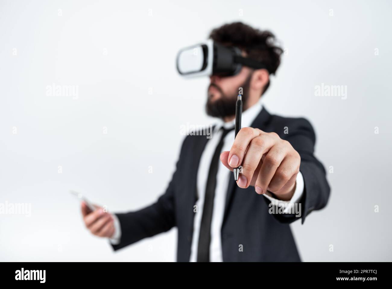 Mann Mit Mobiltelefon, Trägt Eine Vr-Brille Und Zeigt Auf Aktuelle Updates Mit Pen. Ein Geschäftsmann, Der Eine Virtual-Reality-Brille Und Ein Mobiltelefon Besitzt Und Eine Neue Idee Präsentiert. Stockfoto