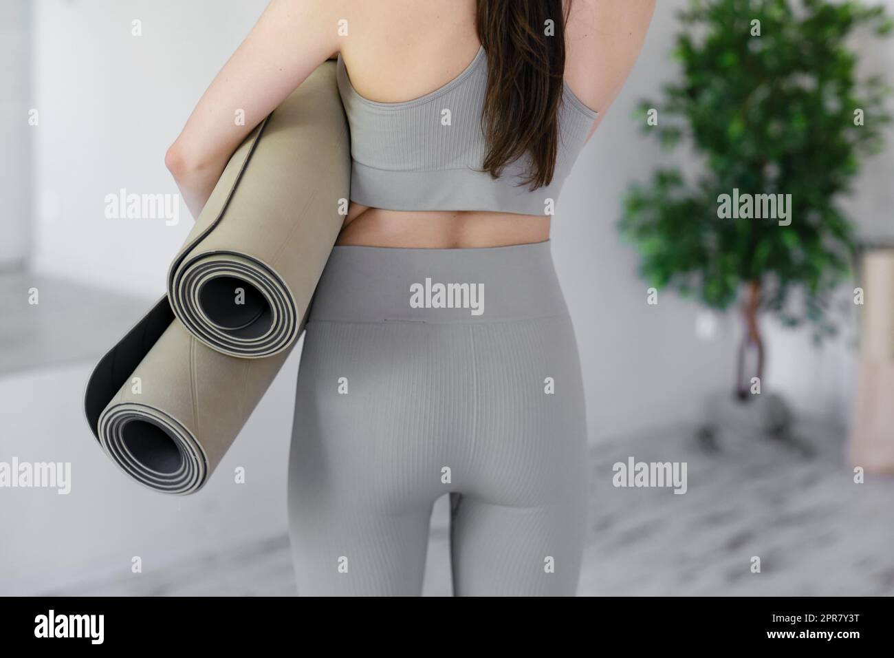 Junge schöne Frau, die Yogamatten hält, während sie in einem hellen Studio steht. Stockfoto