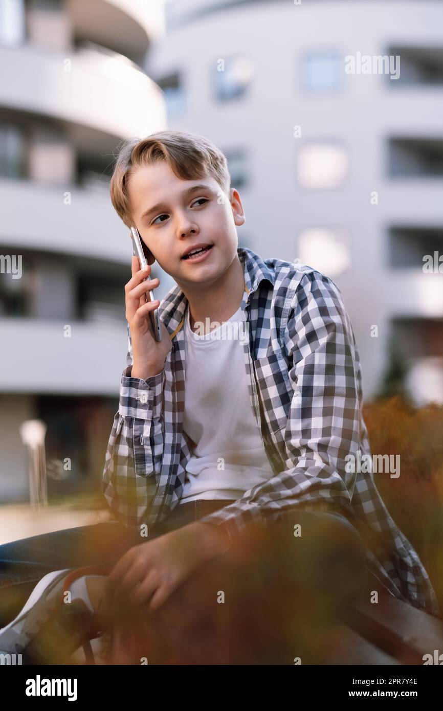 Nahaufnahme eines modernen Teenagers, der mit einem Smartphone spricht, während er auf einer Bank in der Stadt sitzt Stockfoto