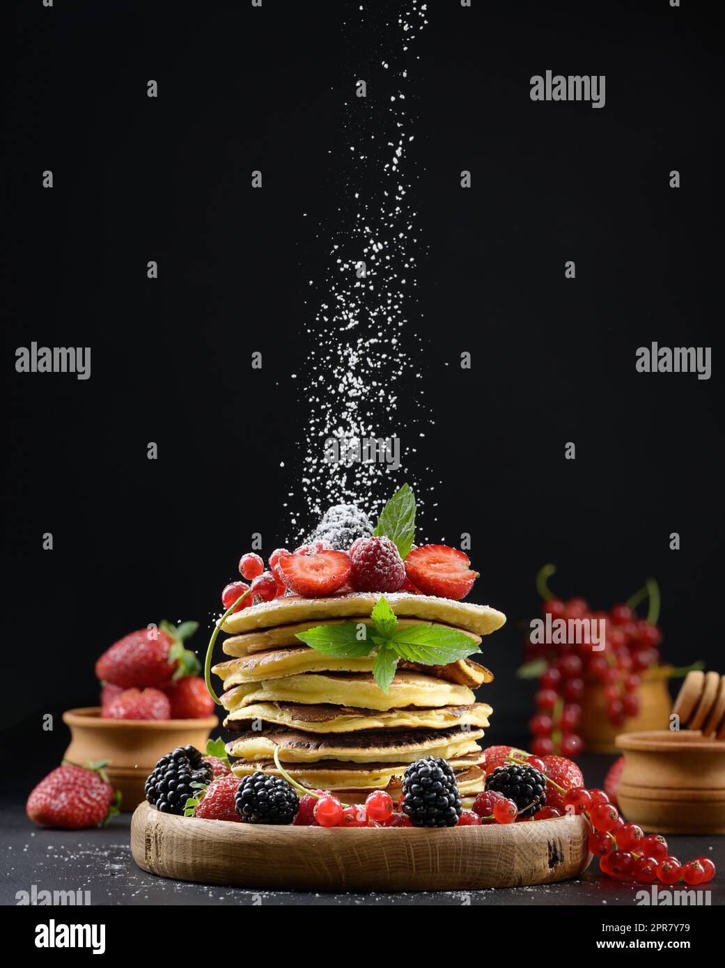 Ein Stapel Pfannkuchen mit frischem Obst, bestreut mit Puderzucker auf schwarzem Hintergrund Stockfoto