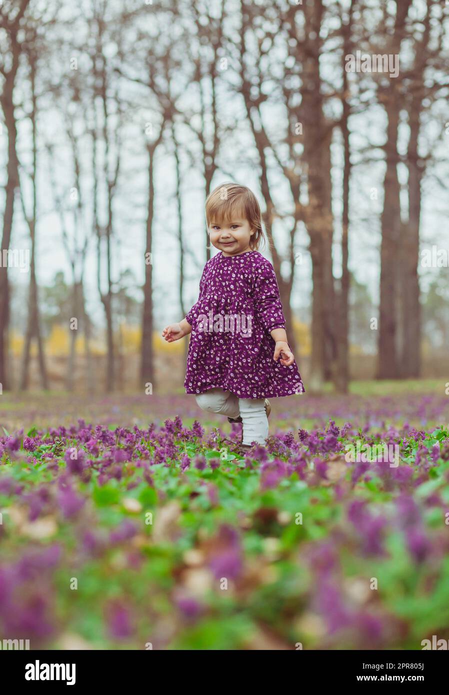 Blondes Baby in einem farbigen Kleid läuft in einer Waldlude mit Blumen Stockfoto