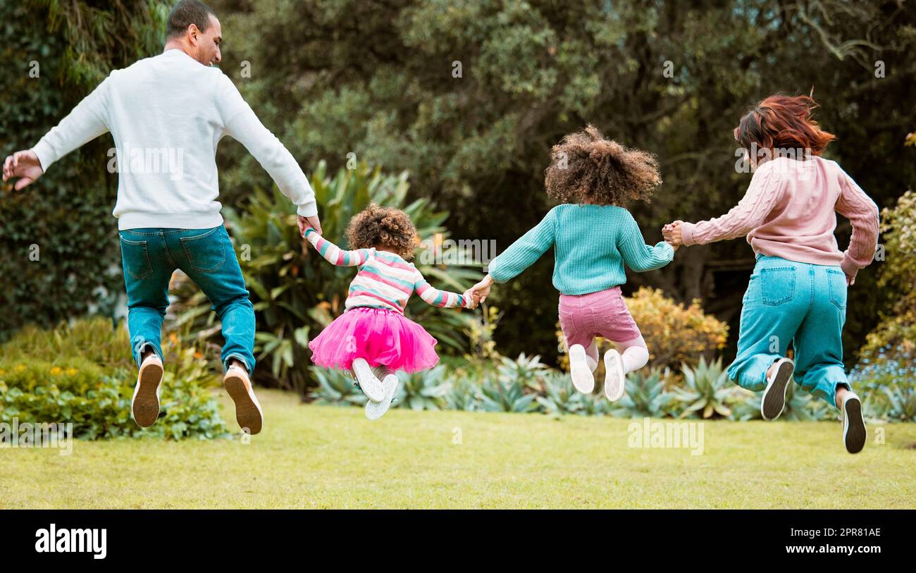Springen Sie vor Freude. Rückansicht einer jungen Familie, die beim Springen nach draußen die Hände hält. Stockfoto