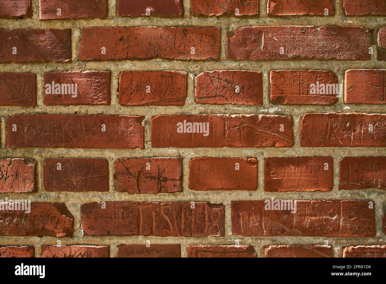 Nahaufnahme einer alten roten Ziegelmauer mit Schnitzereien und Kopierraum. Zoomen Sie auf verschiedene Größen, Formen und Muster von Steinen. Details des Bauwerks mit rauer Oberfläche, skizzierten oder zerkratzten Markierungen Stockfoto
