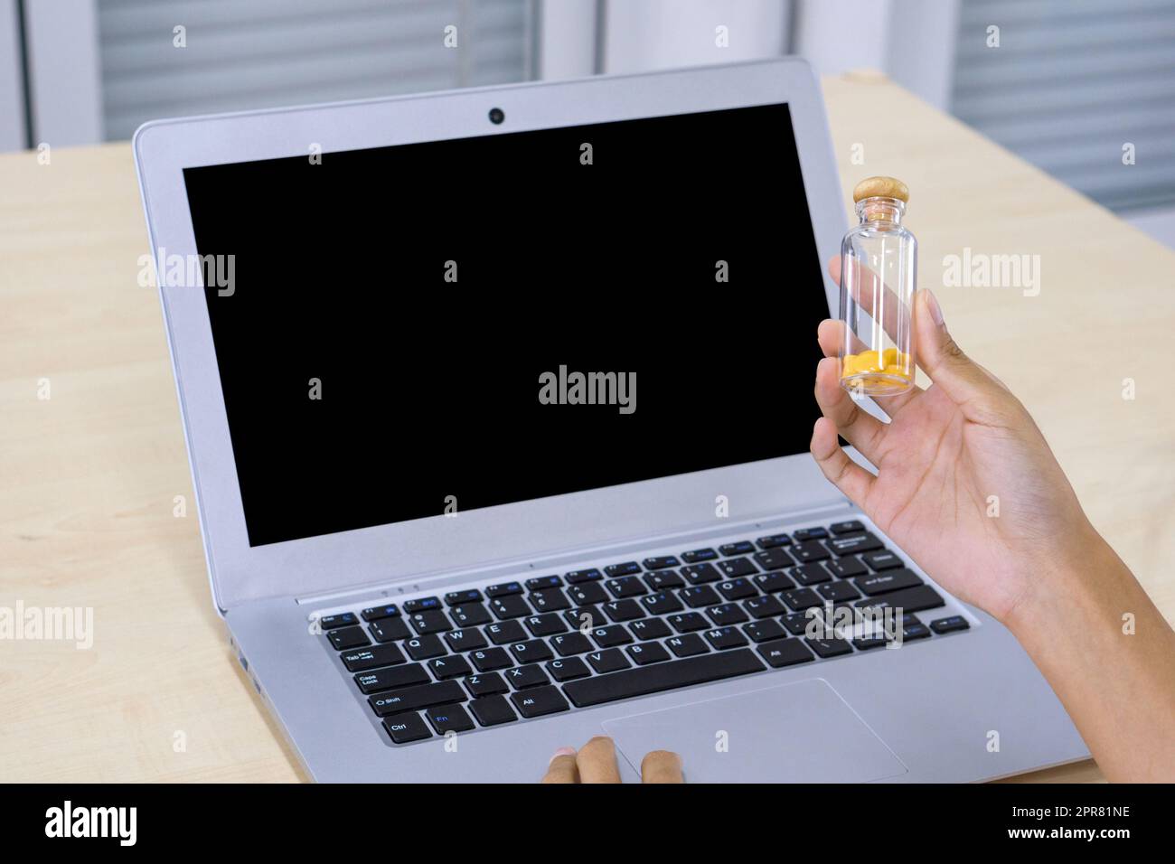 Nahaufnahme Hand hält Glas Pille Packer Flasche mit Holzkappe vor dem schwarzen Bildschirm Laptop-Computer. Stockfoto