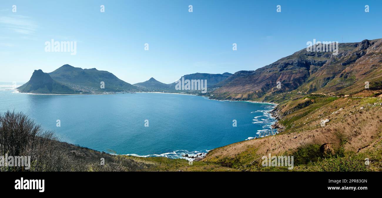 Weitwinkelpanorama der Bergküste vor klarem blauen Himmel in Südafrika. Malerische Landschaft der Twelve Apostles Mountain Range in der Nähe eines ruhigen Ozeans in Hout Bay. Beliebter Wanderort von oben Stockfoto