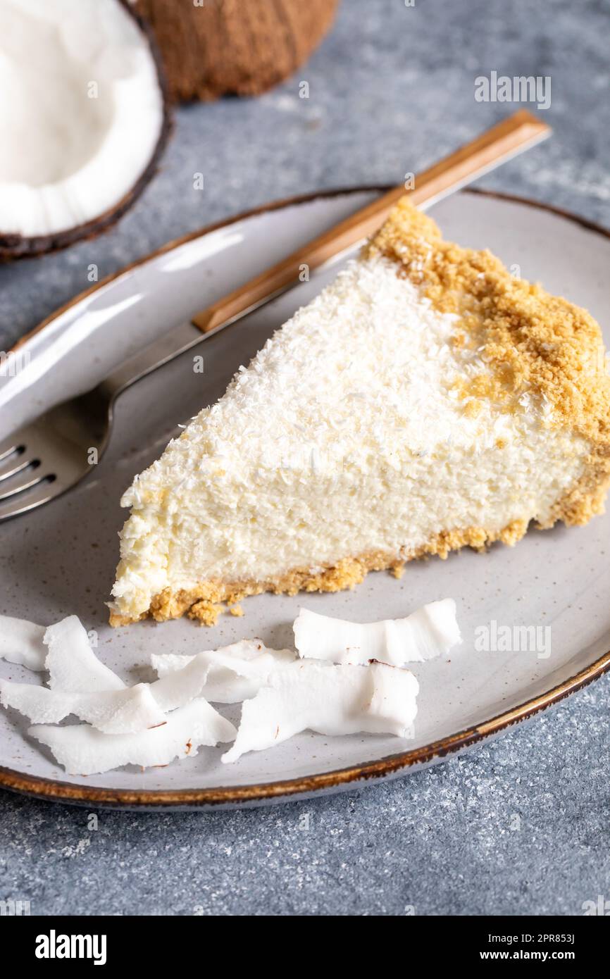 Ein Stück Kokosnuss-Käsekuchen auf einem Teller mit frischer Kokosnuss Stockfoto