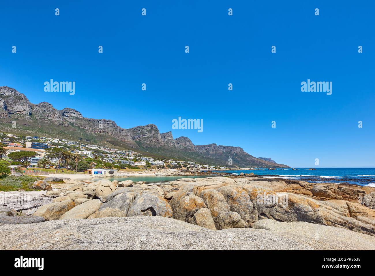 Landschaft eines Sommerurlaubsziels mit einer einzigartigen Bergkette in der Nähe eines felsigen Strandes in Südafrika. Blick auf die zwölf Apostel in Kapstadt und ein ruhiges Meer vor einem hellblauen Horizont. Stockfoto