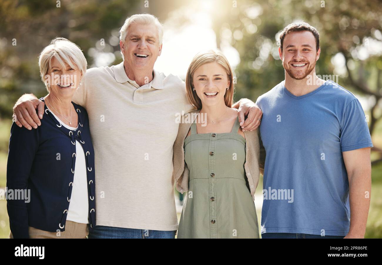 Porträt einer liebevollen weißen Familie mit erwachsenen Kindern, die an einem sonnigen Tag in der Natur zusammenstehen. Glückliches Seniorenpaar, das draußen mit seiner Tochter und seinem Schwiegersohn posiert Stockfoto