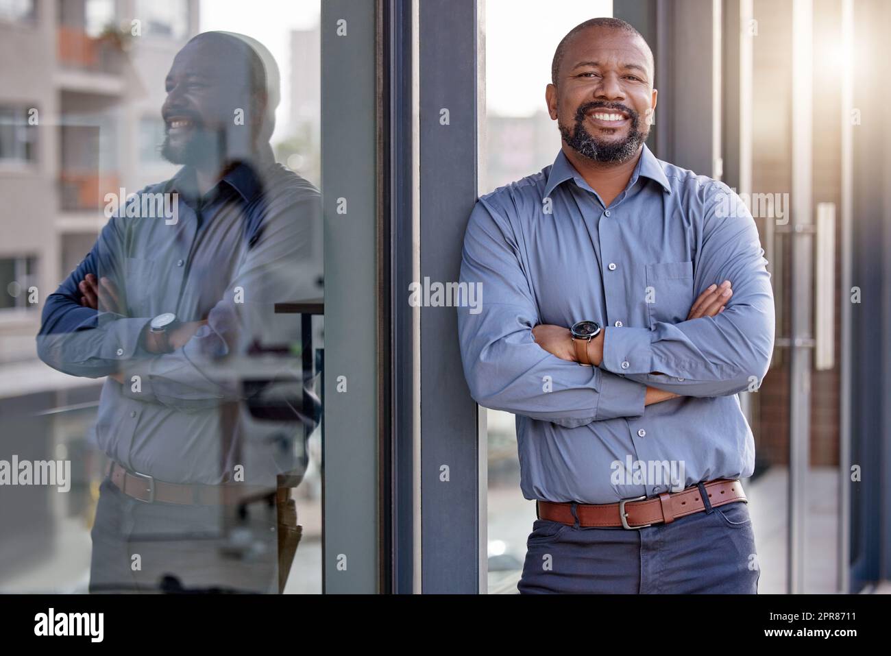 Ein junger Geschäftsmann, der mit gekreuzten Armen vor dem Haus steht. Stockfoto