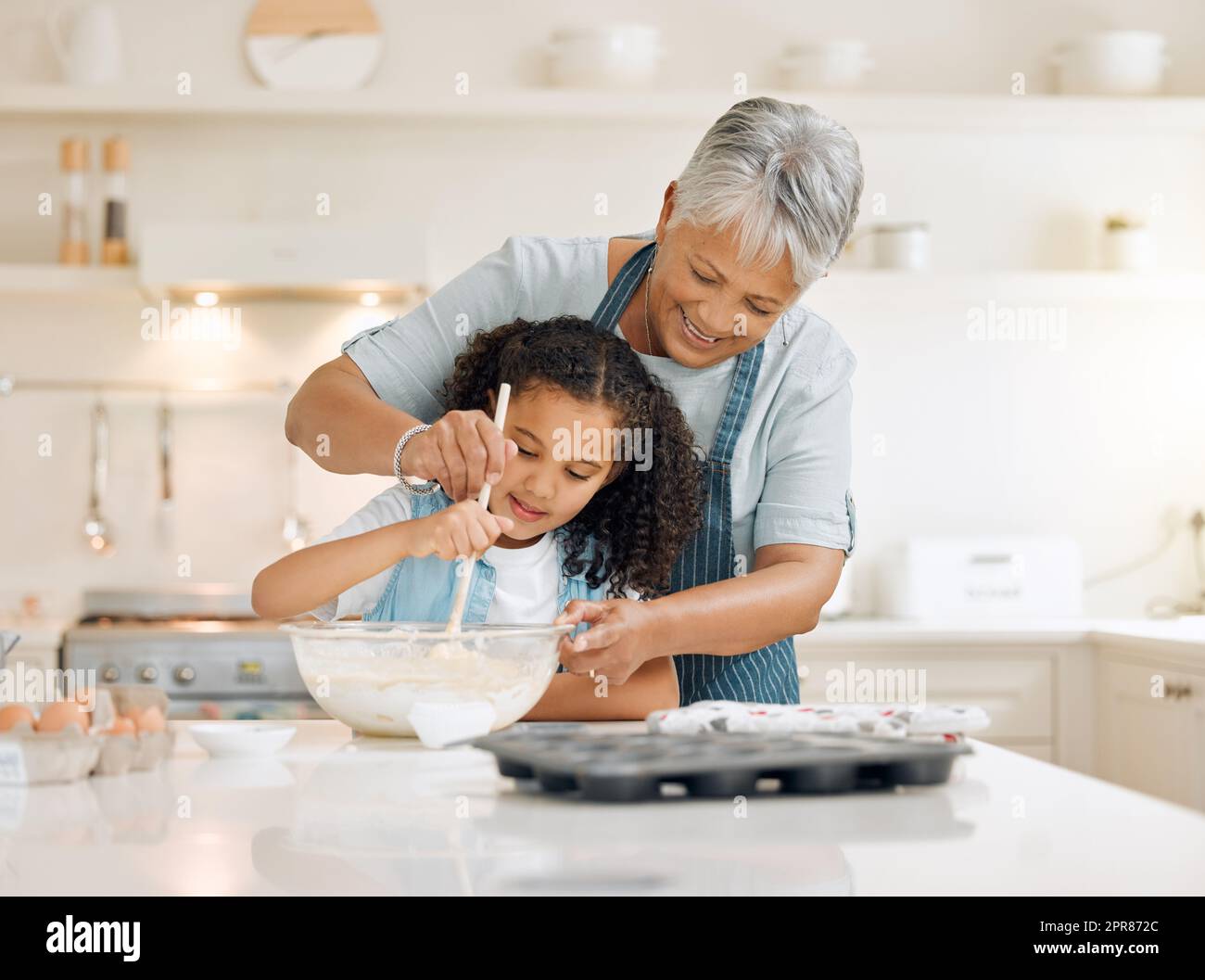 Wir verwechseln die Dinge, wenn es um die Zeit geht. Ein kleines Mädchen, das mit ihrer Großmutter zu Hause backt. Stockfoto