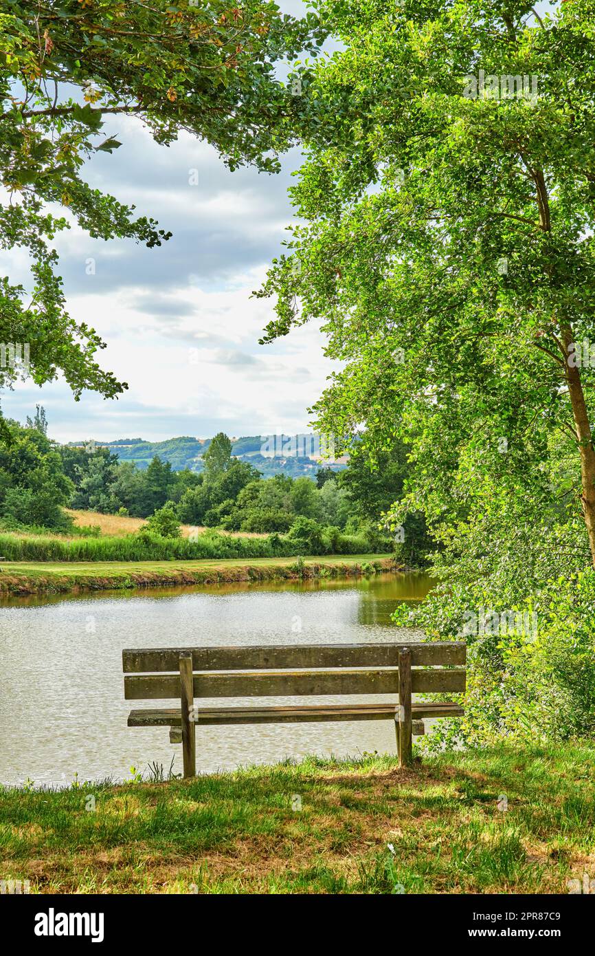 Eine Bank mit Blick auf einen See auf dem Land, umgeben von Ackerland und einem Wald in der Nähe von Lyon, Frankreich. Ein ruhiger Ort zum Entspannen und Nachdenken. Genießen Sie Ruhe und Frieden in der Natur Stockfoto