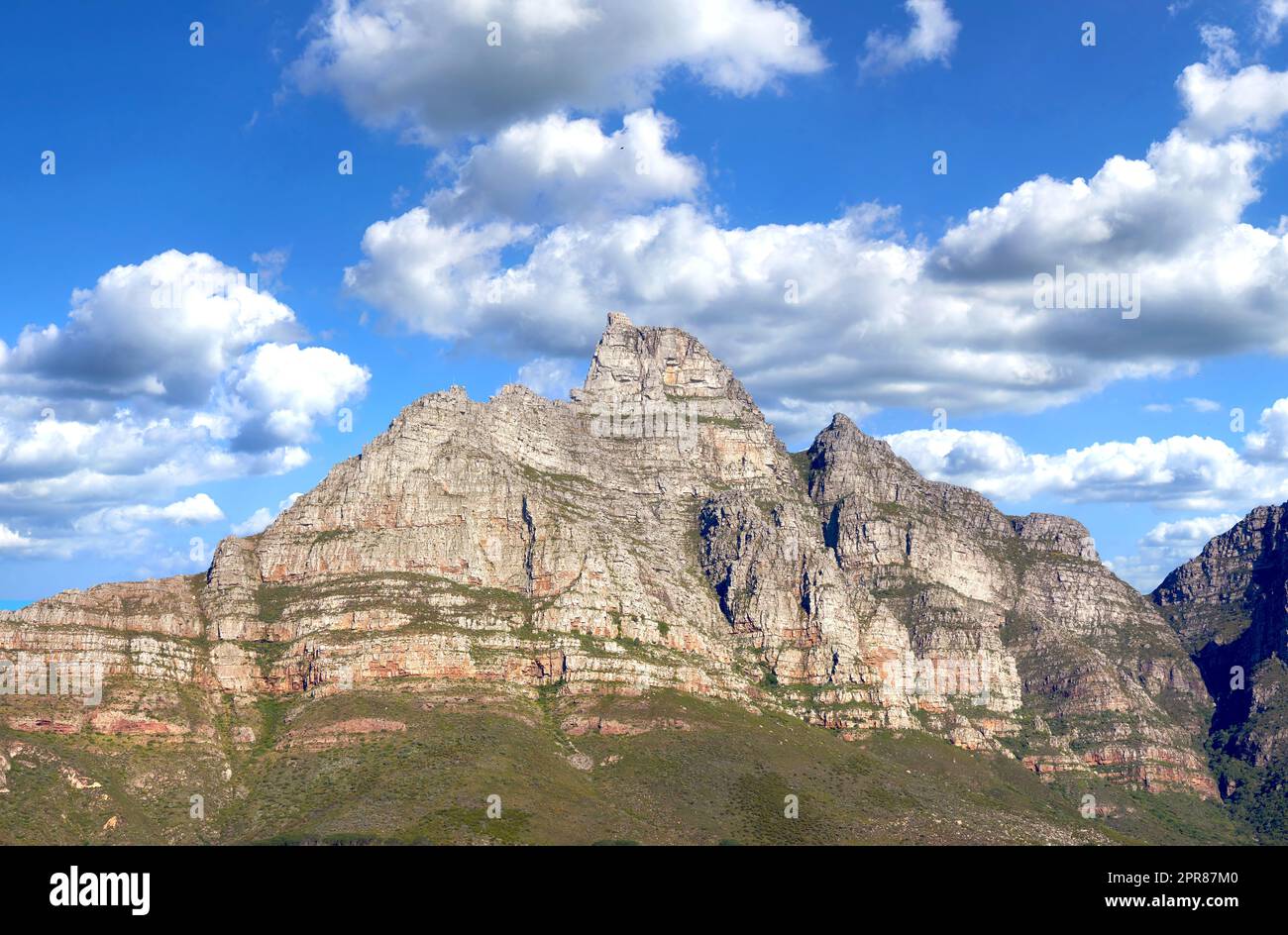 Berglandschaft am blauen, wolkigen Himmel. Wunderschöne Aussicht auf Bergspitzen mit Hügeln bedeckt mit grünem Gras, Sträuchern und Büschen an einem beliebten Wahrzeichen oder Wanderort in Kapstadt, Südafrika Stockfoto