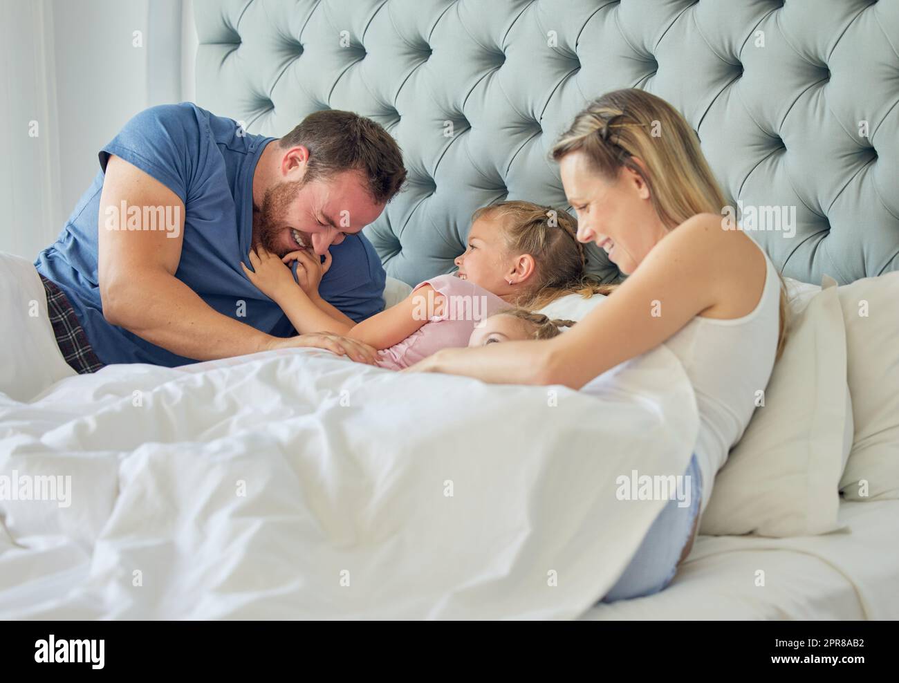 Glückliche weiße Familie, die mit zwei Töchtern im Bett lag. Zwei kleine Mädchen sehen glücklich aus und sind gleichzeitig verspielt und liebevoll mit ihren lächelnden Eltern. Eine vierköpfige Familie in einem großen, komfortablen Bett Stockfoto
